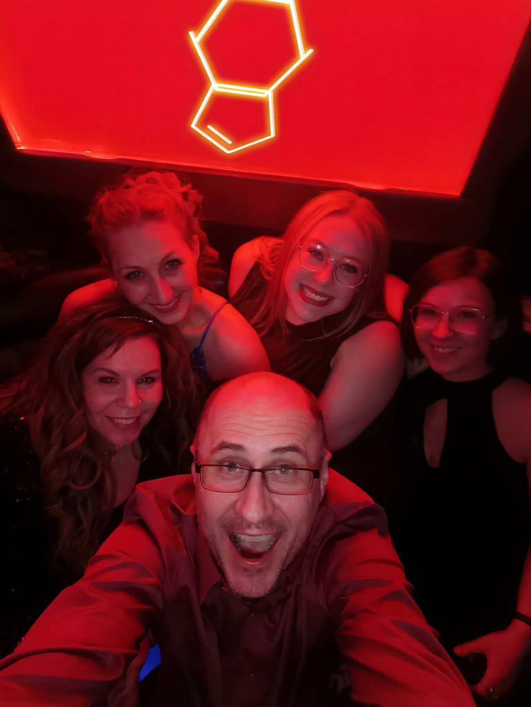PURC founder with friends posing in front of a lit PURC logo